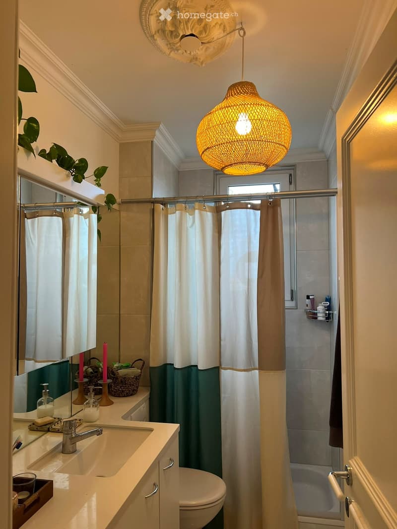 Modern bathroom with a double sink vanity, a toilet, a shower with a curtain, decorative candles, and a woven basket on the counter.