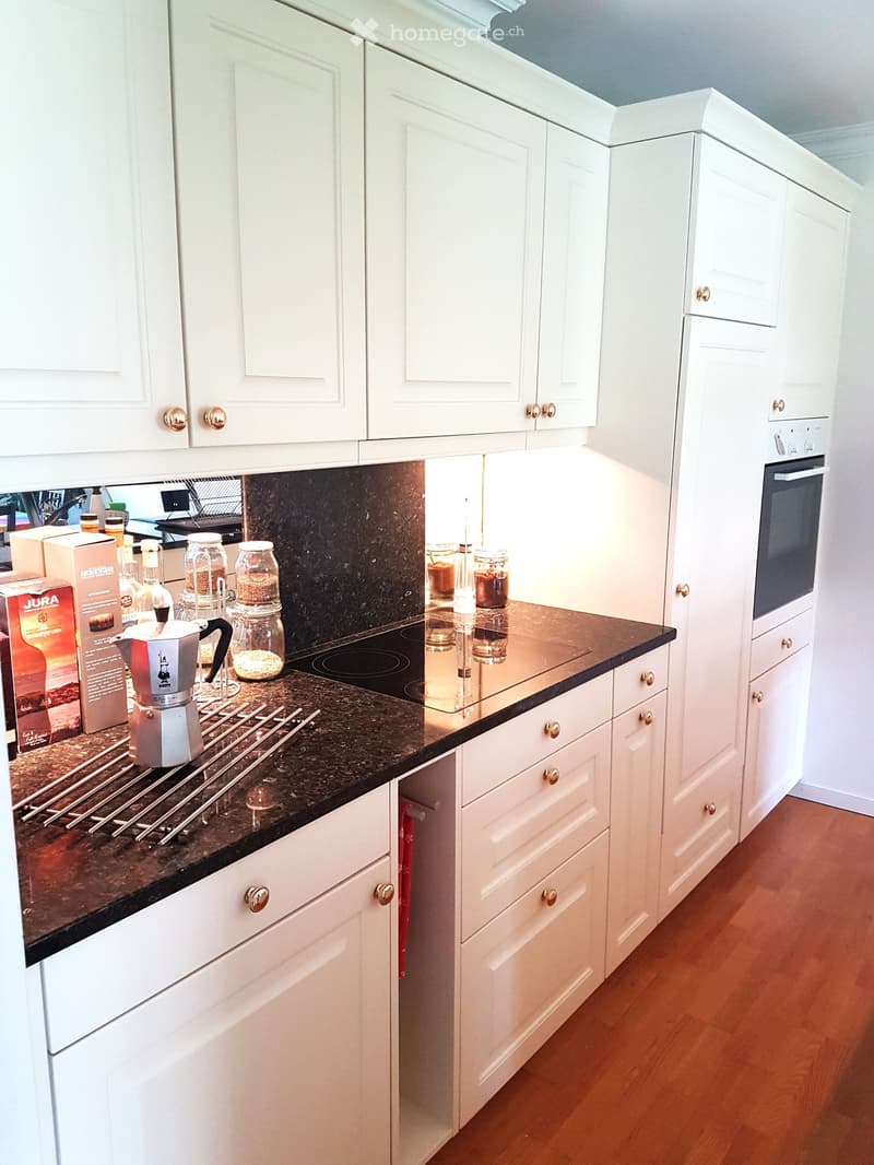 Modern kitchen with white cabinets, dark granite countertop, coffee maker, jars, and an oven.