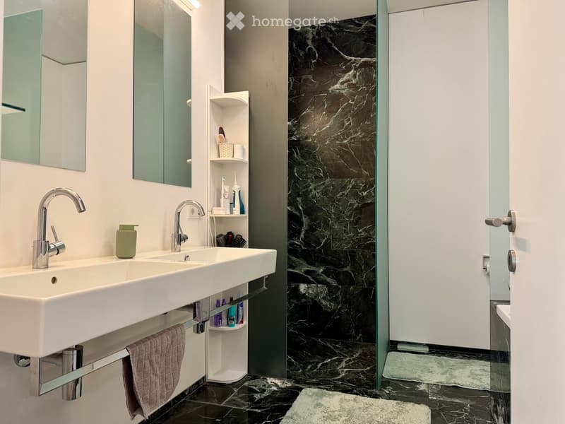 Modern bathroom with double sink, sleek faucets, mirrored cabinet, marble tiles, and a glass-enclosed shower area.