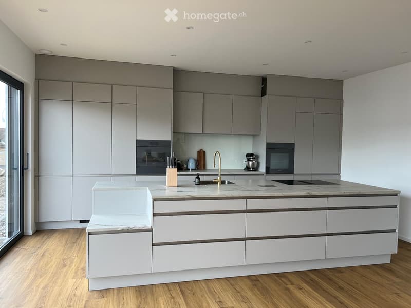Modern kitchen with grey cabinets, white island, marble countertop, and stainless steel appliances.