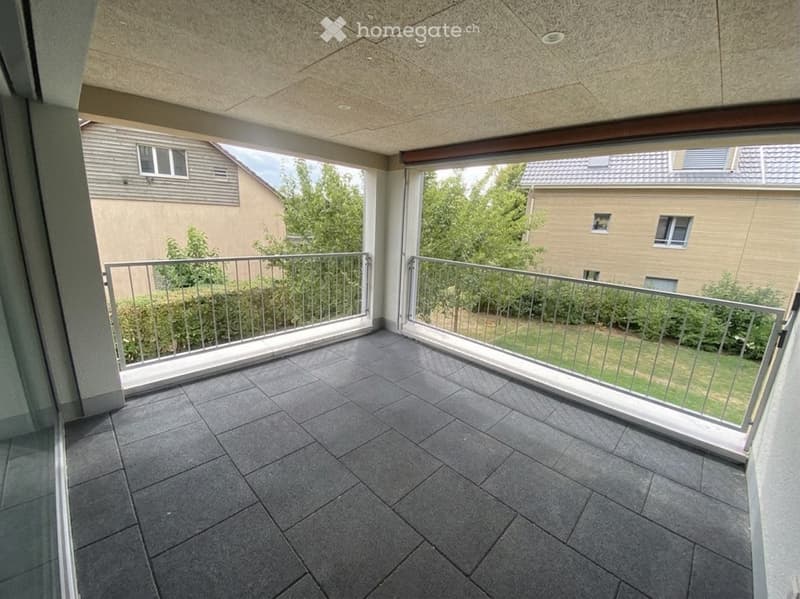 Balcony with dark grey tiled floor, metal railing, and view of neighboring buildings and greenery.