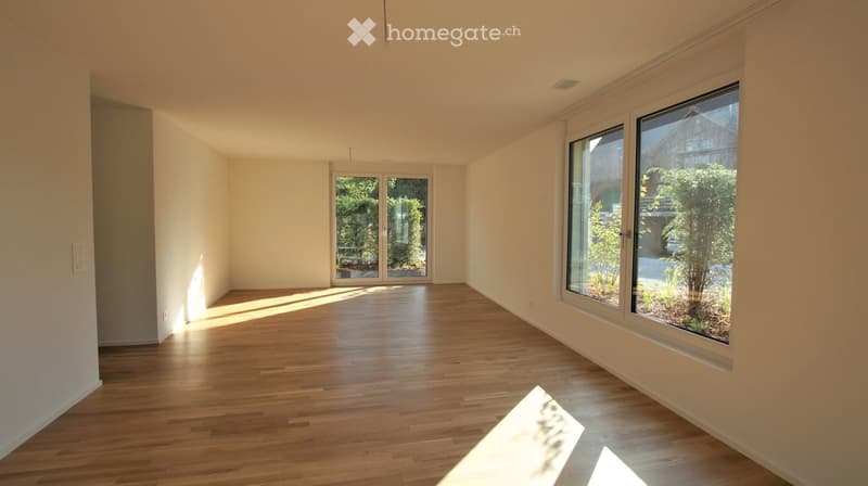 Empty room with wooden flooring, large windows, and a sliding glass door leading to an outdoor area.