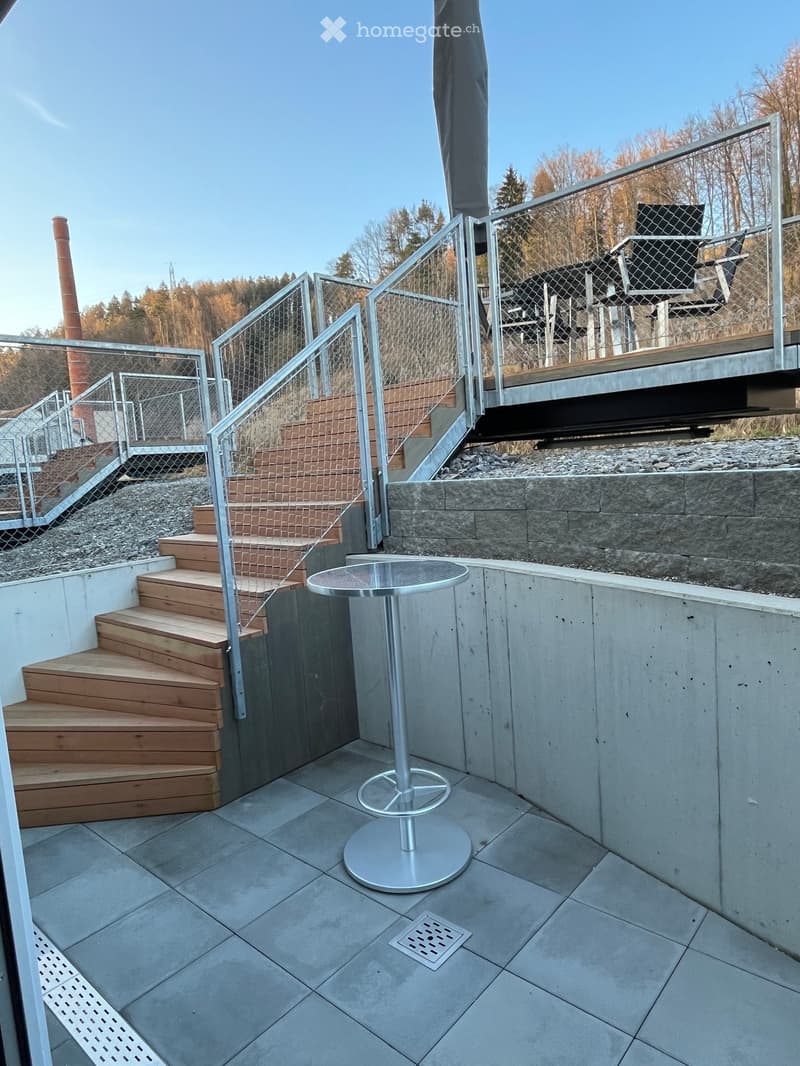 Modern balcony with tiled floor, wooden steps, metal railing, and a round table.