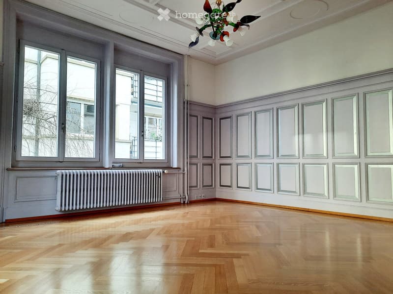 Wooden parquet floor, large windows, paneled walls, radiator, decorative ceiling light