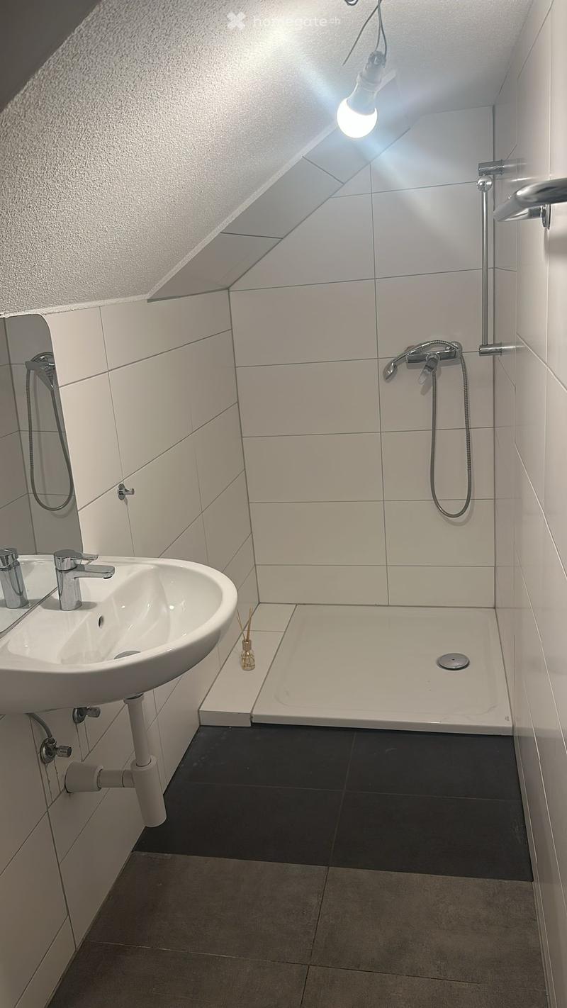 Modern bathroom with white tiles, a sink with a chrome faucet, a bathtub with a handheld showerhead, and a mirror. The room features a sleek, contemporary design with a recessed ceiling light.
