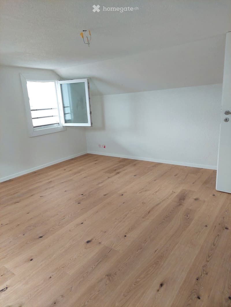 Empty room with wooden flooring and white walls, featuring a window with white frame and a door on the right side.