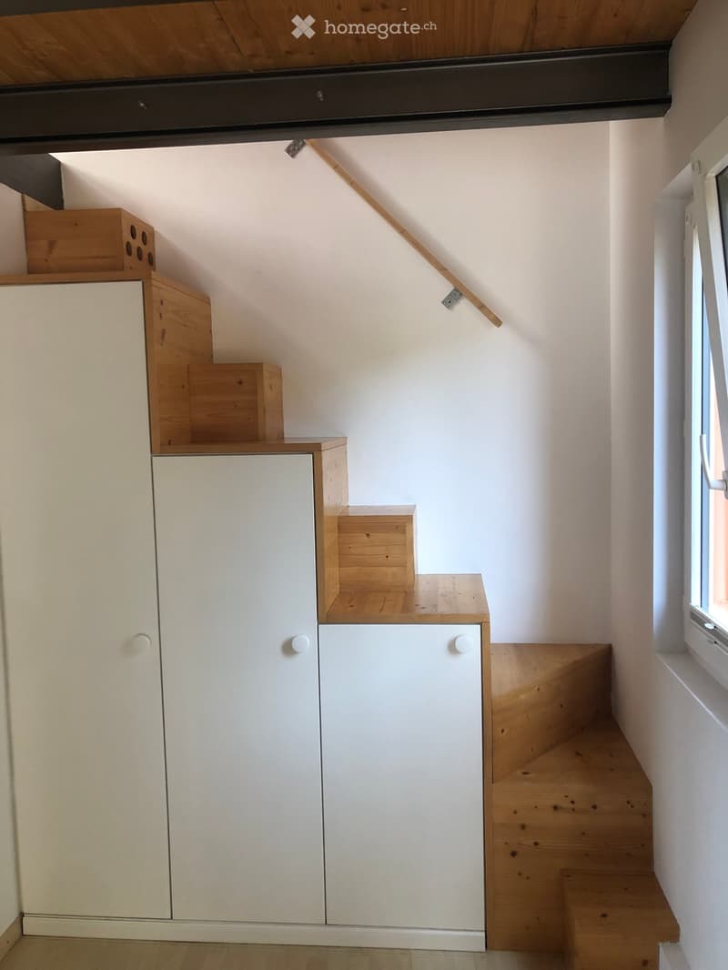 Modern hallway with wooden staircase, white built-in storage cabinets, and a window on the right side.