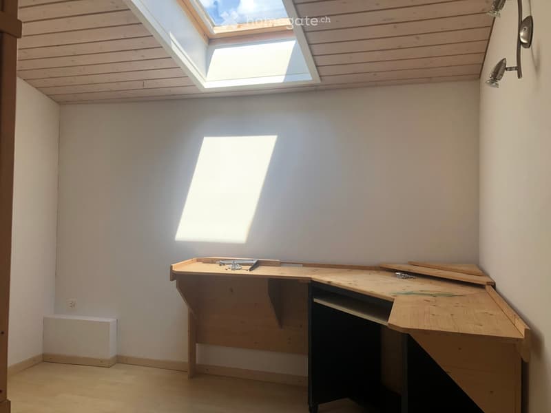 Empty room with wooden floor, white walls, skylight window, and a wooden workbench with tools.