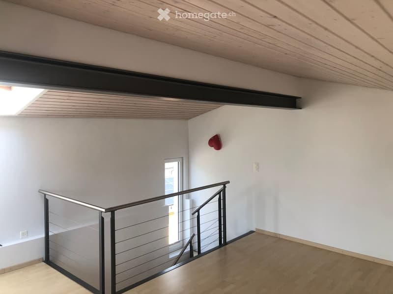 Empty hallway with wooden flooring, white walls, and a modern glass railing leading to a bright room.