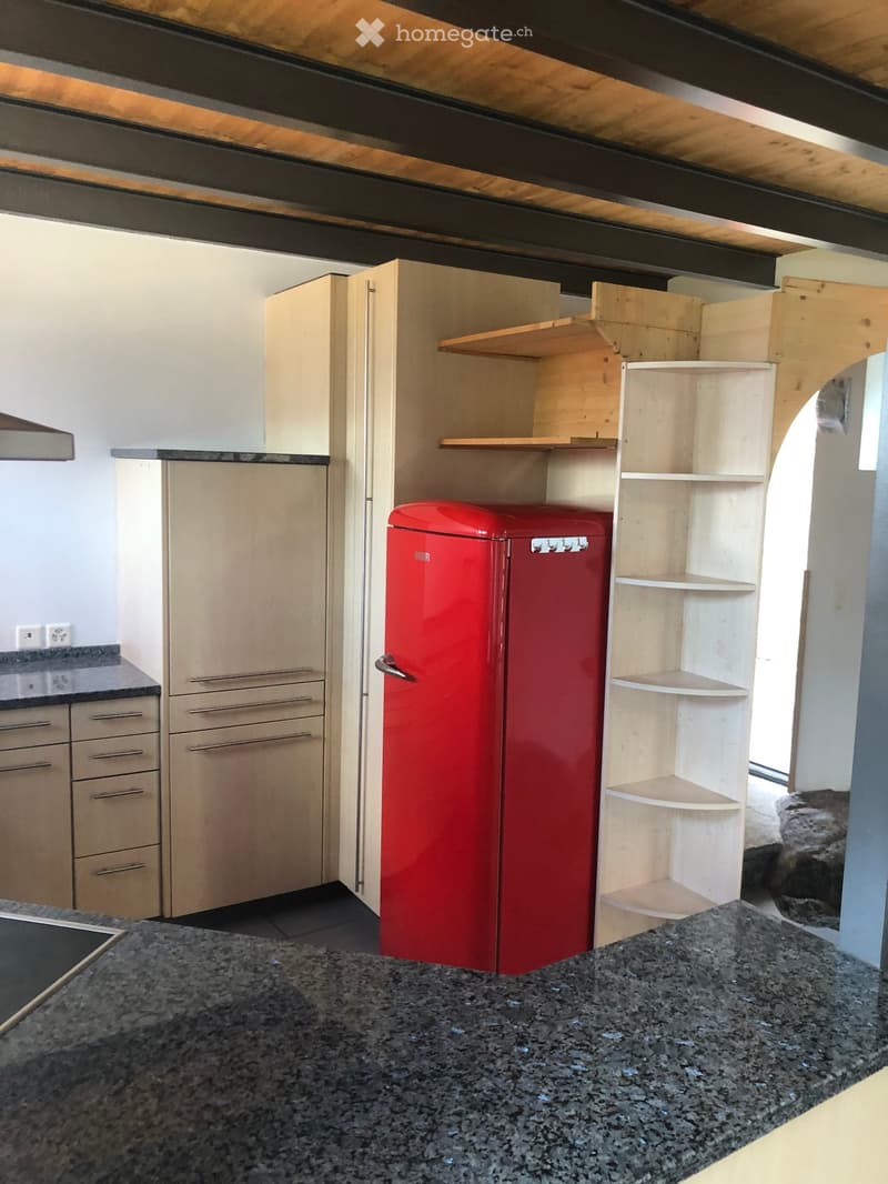 Modern kitchen with light wooden cabinets, a red refrigerator, and a granite countertop.