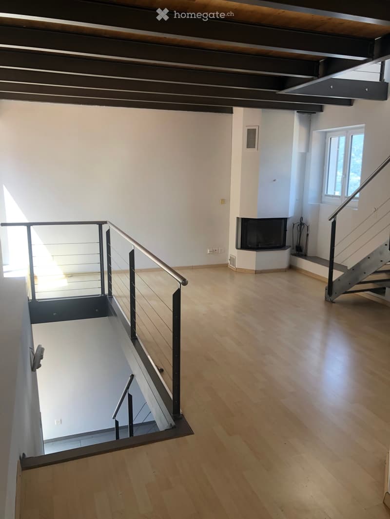 Open, airy hallway with wooden flooring, white walls, and a modern metal staircase leading upwards. Features a built-in fireplace and large windows allowing natural light.