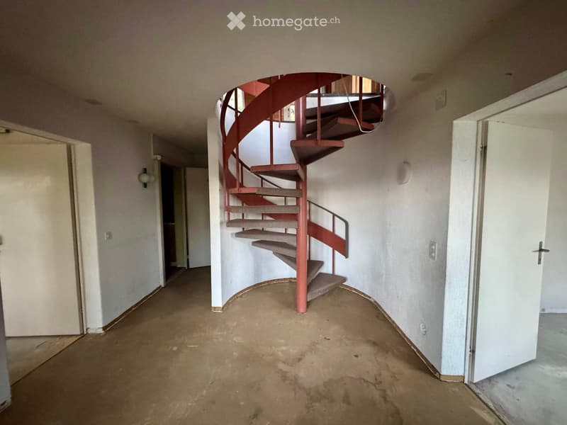 Empty hallway with a spiral staircase leading upwards, unfinished walls, and open doors on either side.
