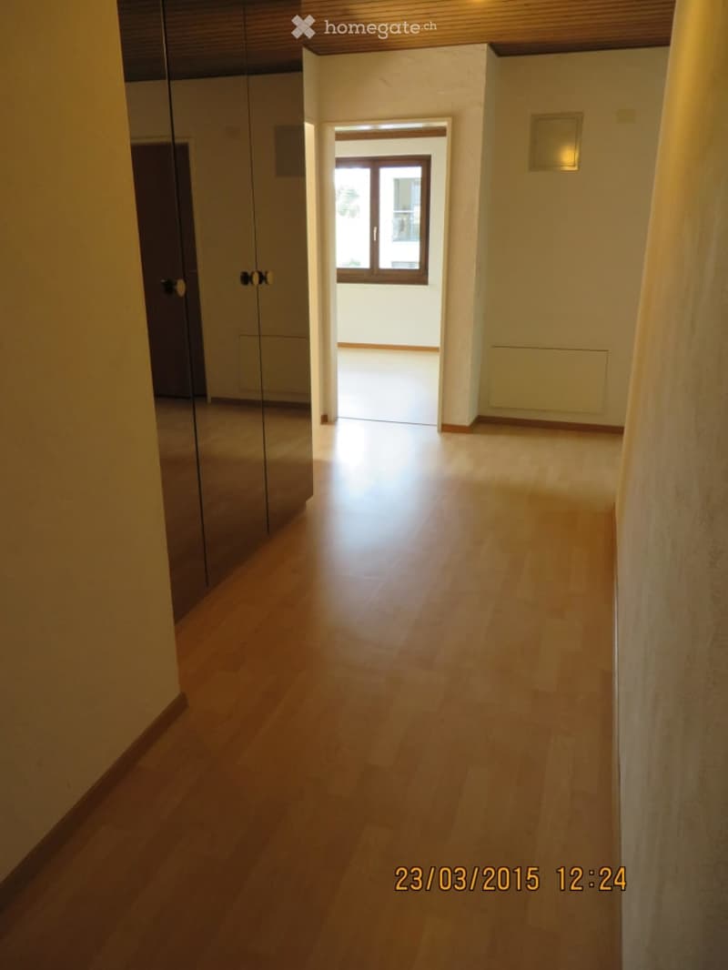Empty hallway with wooden flooring, white walls, and a large window at the end. No furniture or equipment is present.
