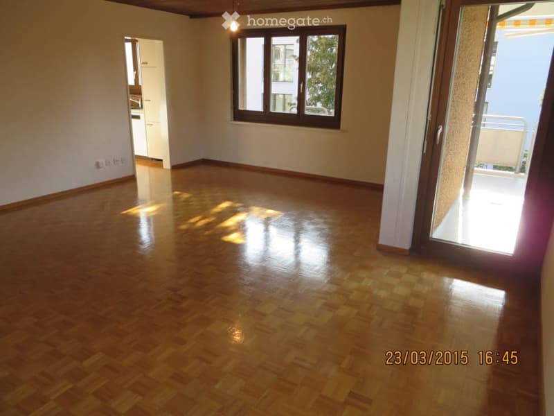Empty room with polished wooden flooring, large window, and open sliding door leading to a balcony.