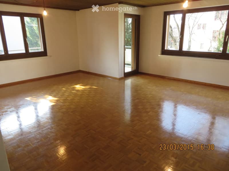 Empty room with wooden flooring, white walls, large windows, and a door leading outside.