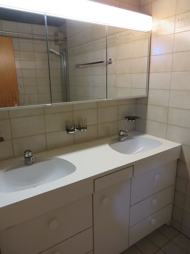 Bathroom with double sink vanity, large mirror with built-in lighting, and two cups on the counter.