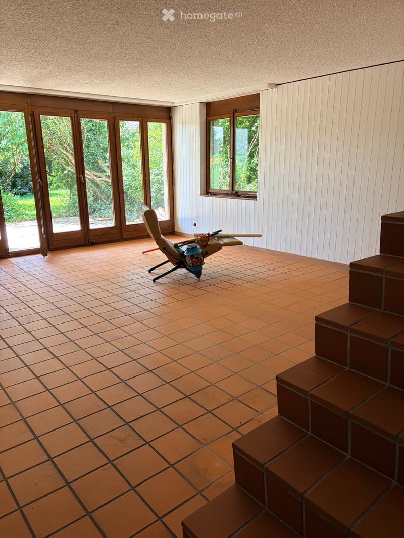 Empty room with tiled floor, large windows, and a staircase leading upwards. No furniture or equipment present.
