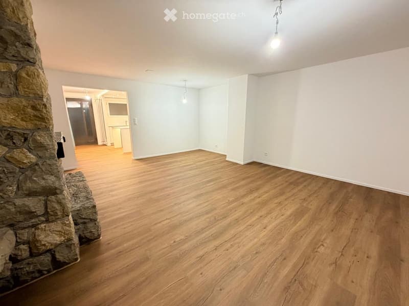 Empty room with wooden flooring, light-colored walls, and a stone fireplace. No furniture or equipment is present.