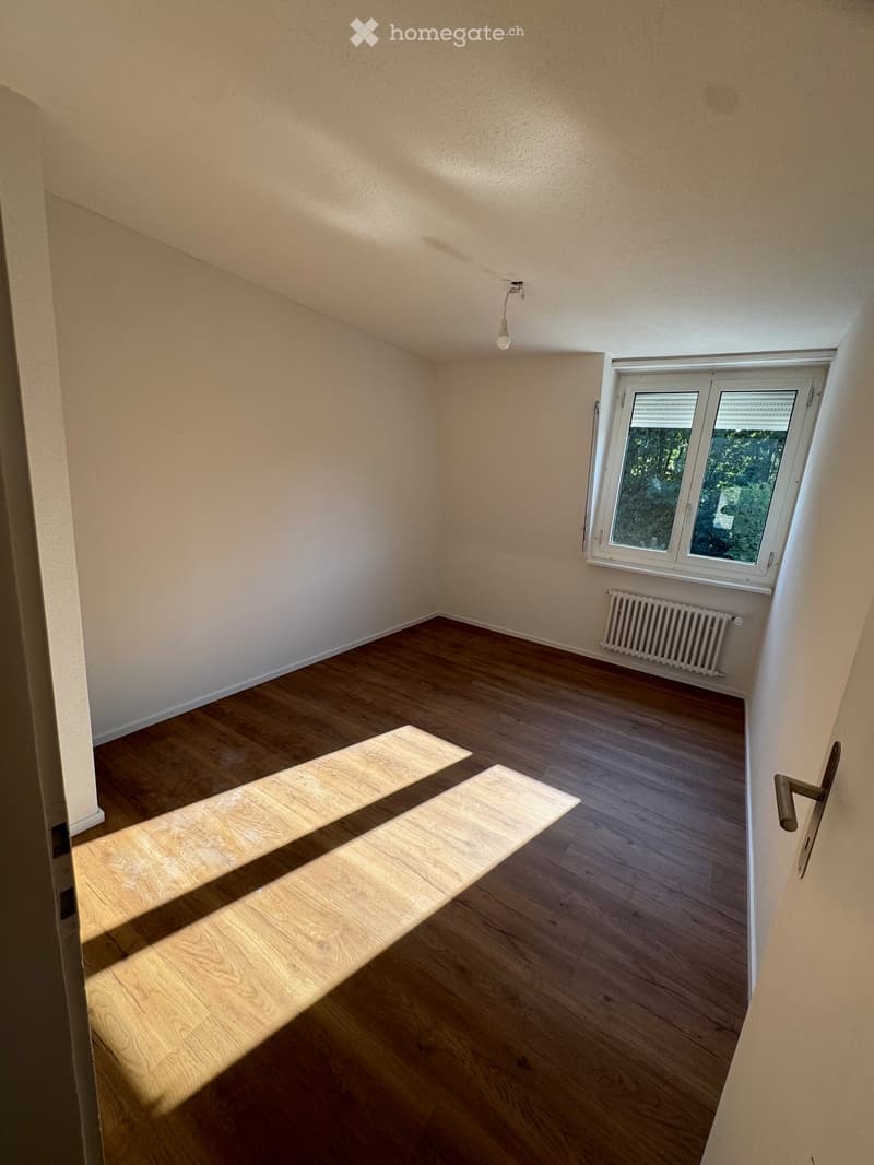 Empty room with wooden flooring, white walls, a window with blinds, and a radiator. No furniture or equipment present.