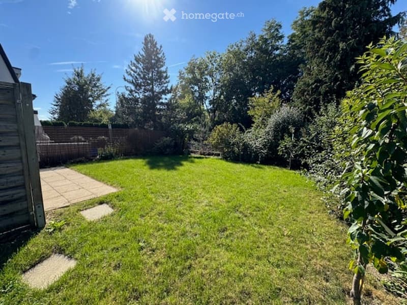 Well-maintained garden with a neatly trimmed lawn, a wooden fence, and a paved patio area. The garden is surrounded by trees and shrubs, providing a private and serene outdoor space.