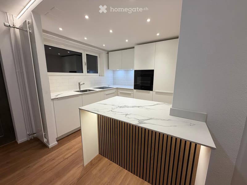 Modern kitchen with white cabinets, marble countertop, sink, faucet, and built-in oven. Features wooden flooring and large windows.