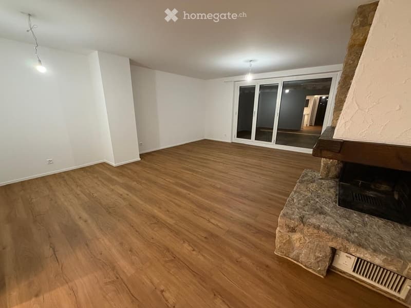 Empty room with wooden flooring, white walls, and a stone fireplace. Large sliding glass doors lead to another space.
