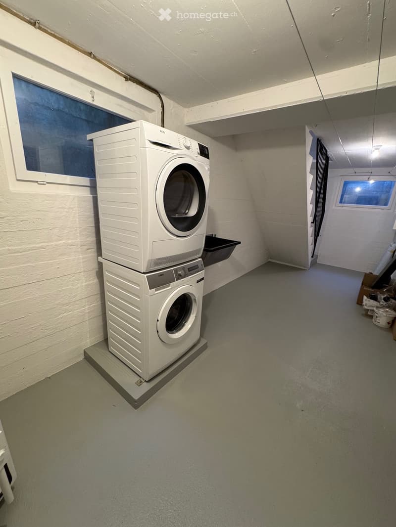 A small utility room with a stacked washing machine and dryer unit, white walls, and a concrete floor.