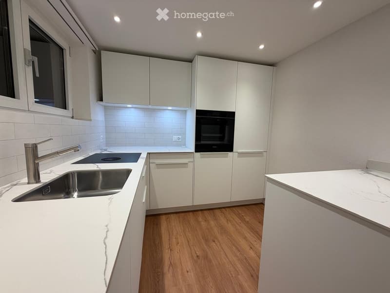 Modern kitchen with white cabinets, marble countertops, stainless steel sink, and built-in oven.