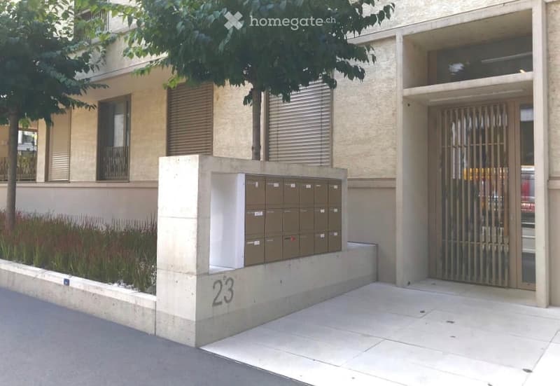 Modern building entrance with mailboxes, small garden, and a gated door.