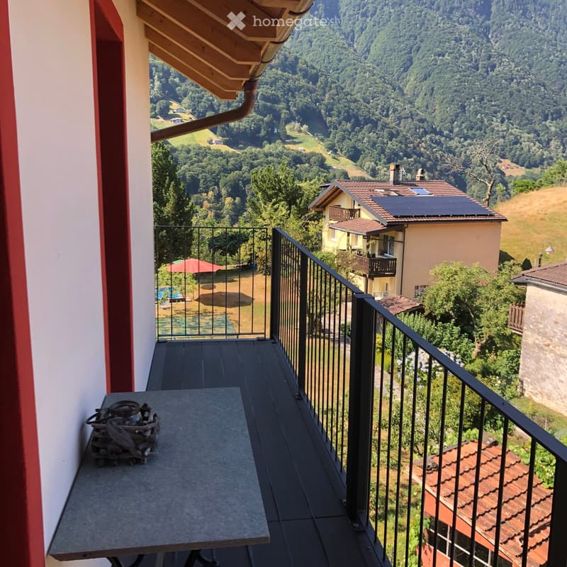 Balcony with a table and a scenic view of a hilly, forested landscape with houses and solar panels.