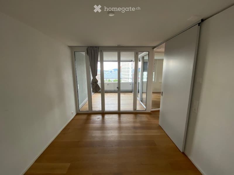 Empty room with wooden flooring, large sliding glass doors leading to a balcony, and white walls.