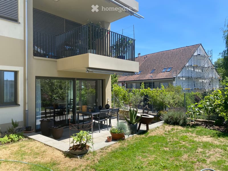 Garden area with a patio, outdoor dining table and chairs, potted plants, and a well-maintained lawn.