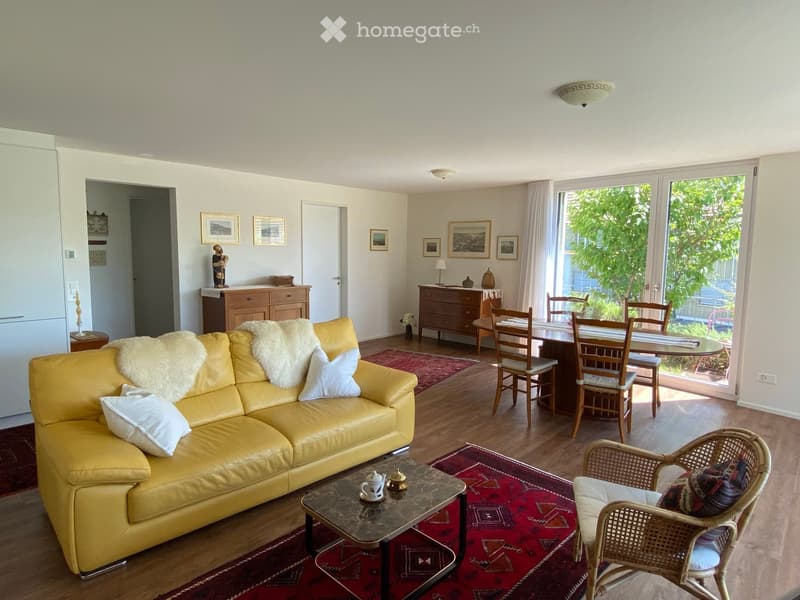 Bright living room with a yellow leather sofa, coffee table, dining area with chairs and table, and decorative items including picture frames and a cabinet.