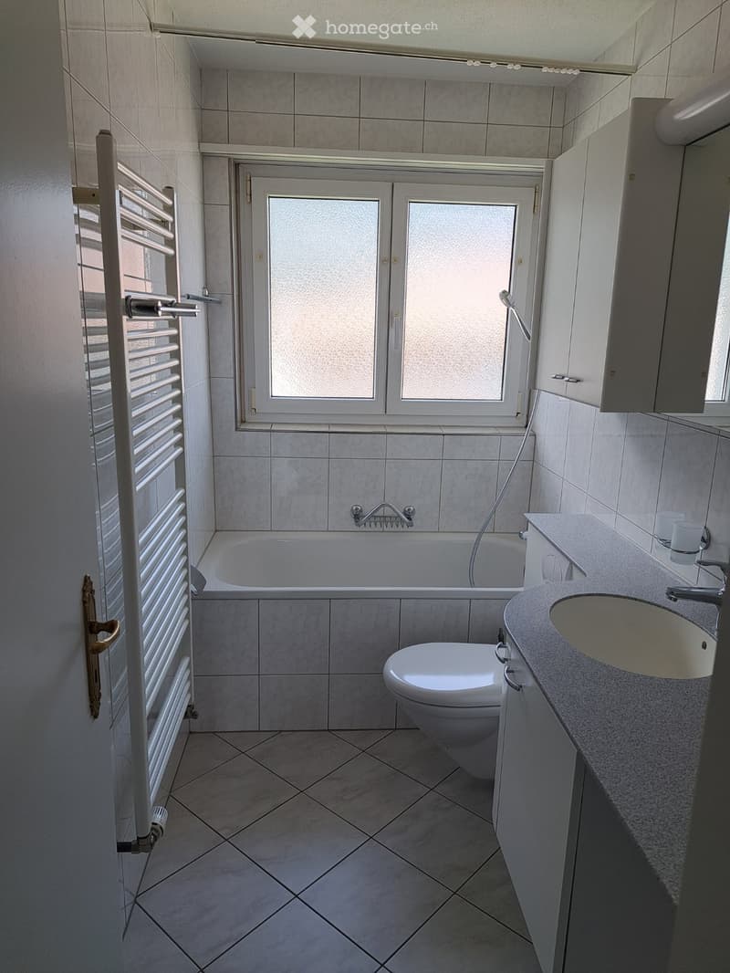 Modern bathroom with tiled walls and floor, featuring a bathtub, toilet, sink, and radiator.