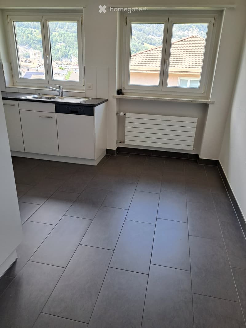Modern kitchen with grey tiled floor, white cabinets, sink, faucet, dishwasher, and radiator.