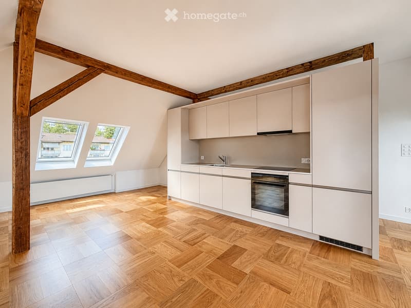 Modern kitchen with light-colored cabinets, wooden herringbone flooring, and skylight windows. Features a sink, faucet, and built-in oven.