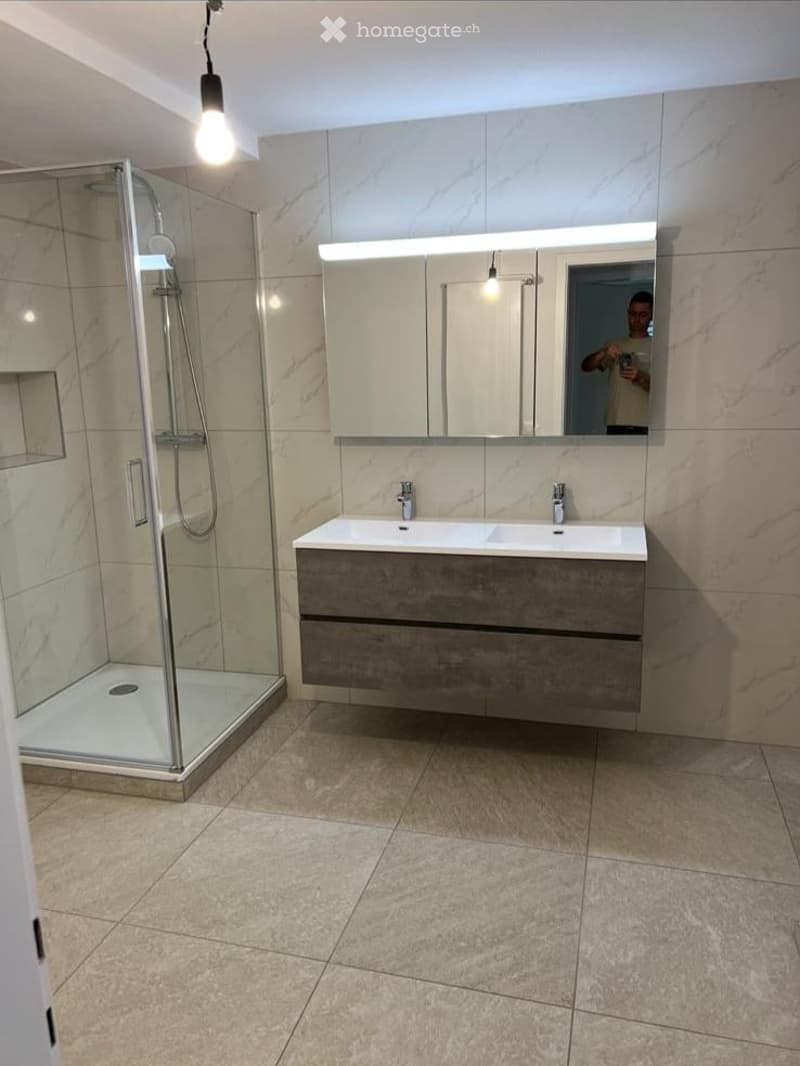 Modern bathroom with a double sink vanity, large mirror, glass-enclosed shower, and tiled floors.
