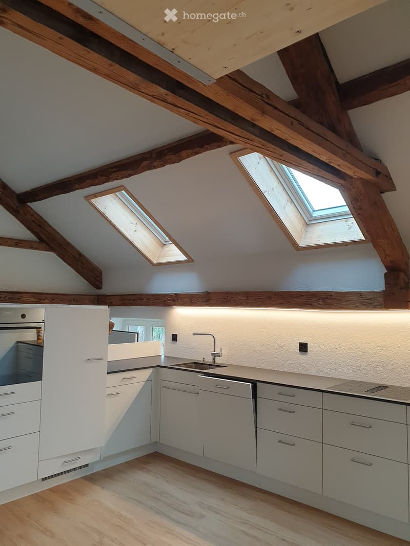 Modern kitchen with white cabinets, stainless steel sink, and exposed wooden beams on the ceiling. Two skylights provide natural light.