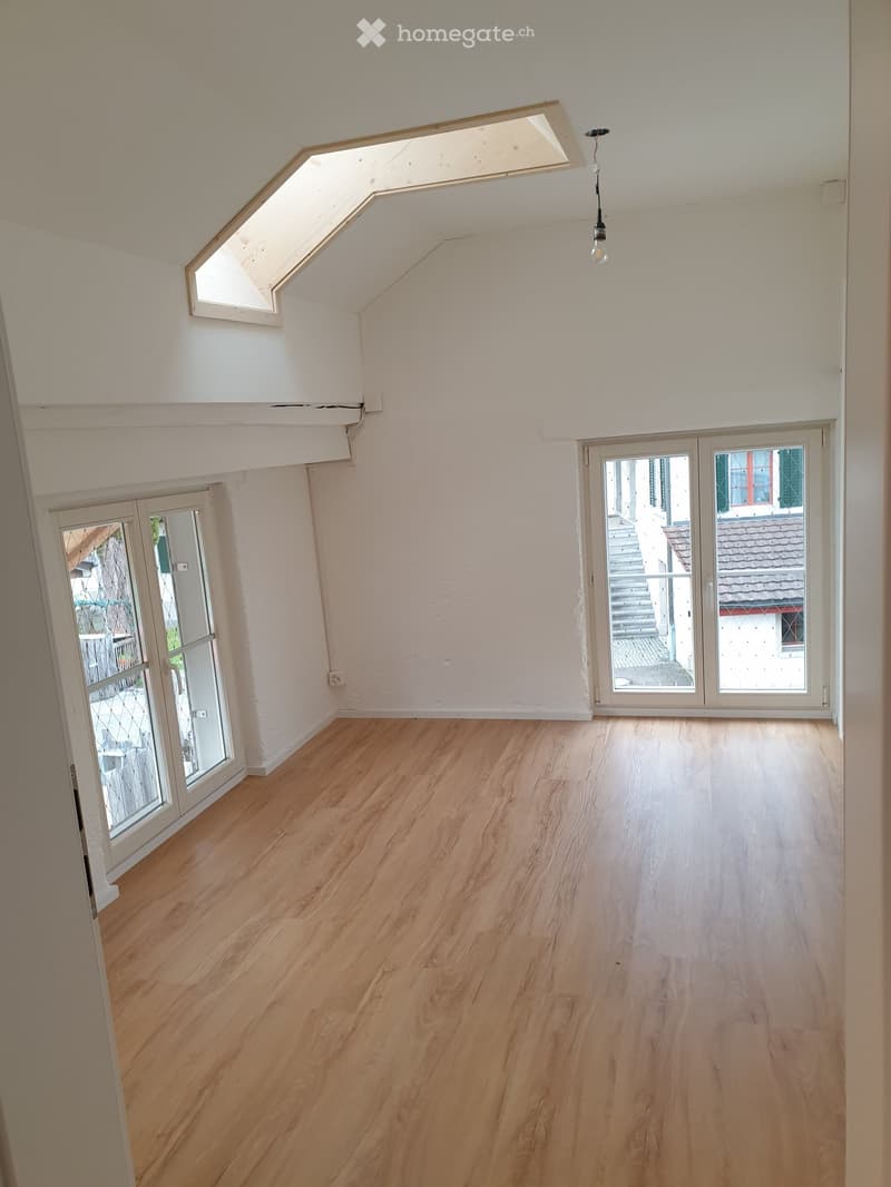 Empty room with wooden flooring, white walls, and large windows with glass doors leading to a balcony.