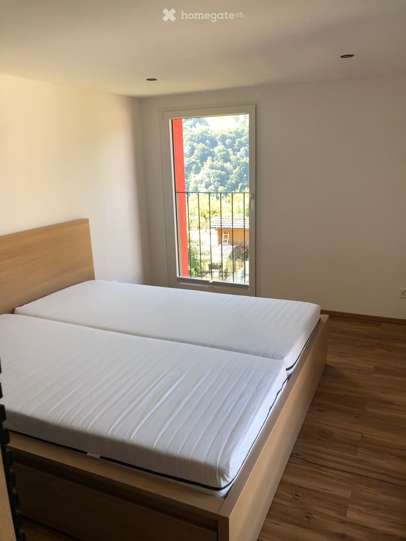 Bright bedroom with two single beds, wooden headboards, and a large window with a view of greenery and a balcony.