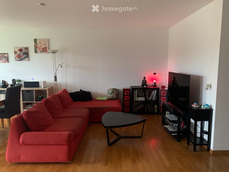 Modern living room with a red sectional sofa, black coffee table, wooden floor, bookshelf, and decorative items.