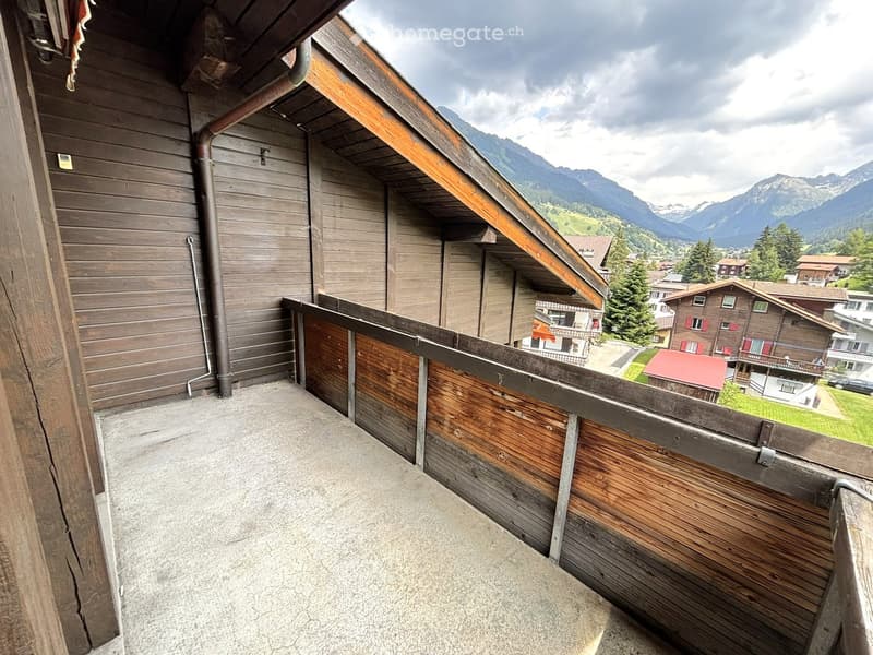 Balcony with wooden railing, overlooking a village with traditional wooden houses and distant mountains.