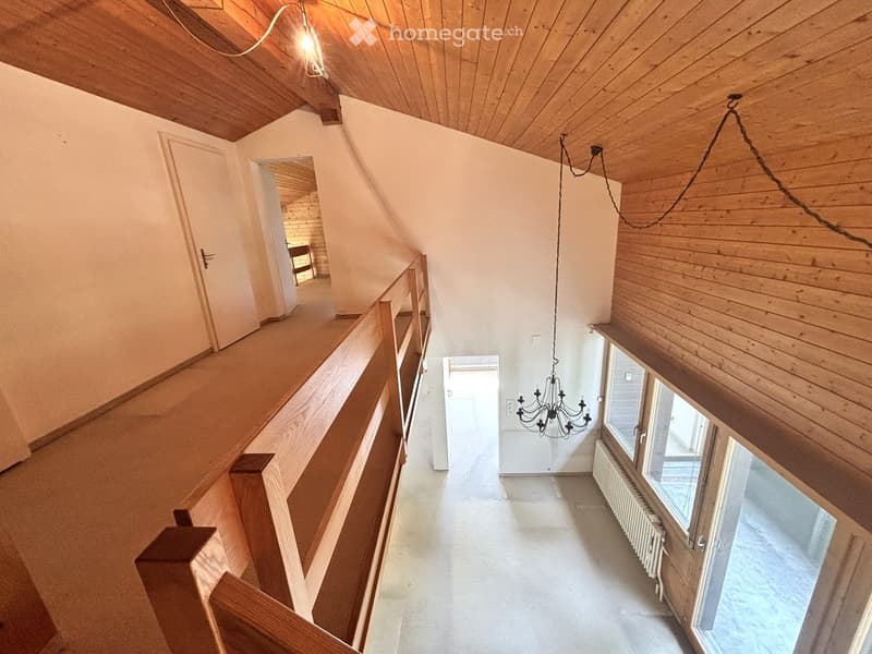 Spacious hallway with wooden ceiling, white walls, and large windows, featuring a staircase with wooden railings and a chandelier hanging from the ceiling.