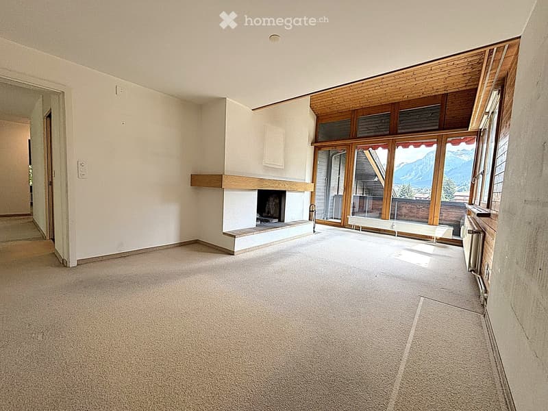 Empty room with carpeted floor, white walls, fireplace with wooden mantel, large windows with mountain view, and a doorway leading to another space.