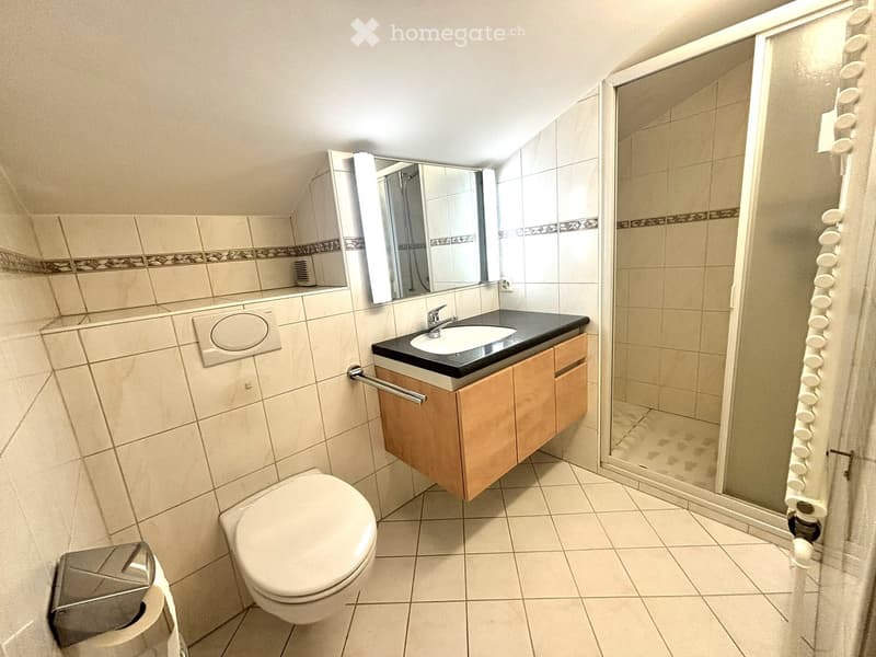 Modern bathroom with beige tiles, a toilet, a sink with a wooden cabinet, a mirror, and a glass-enclosed shower area.