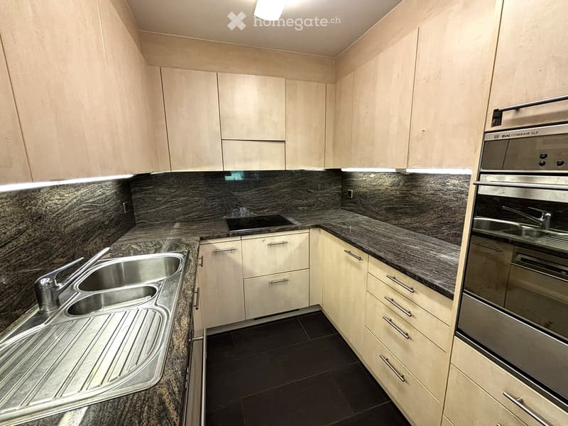 Modern kitchen with light wood cabinets, granite countertops, stainless steel sink, and built-in oven.