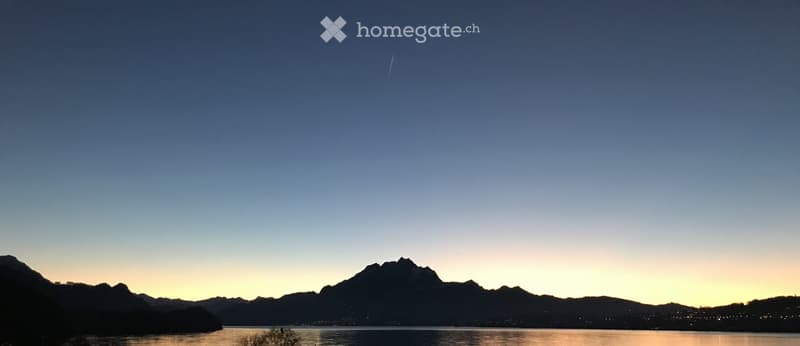 a lake, silhouetted mountains, town lights, and the setting sun