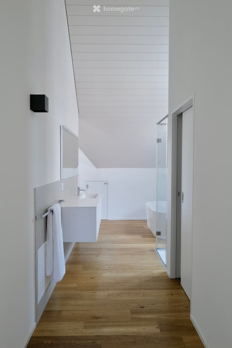 Modern bathroom with white walls, wooden floor, sink, bathtub, and mirror.