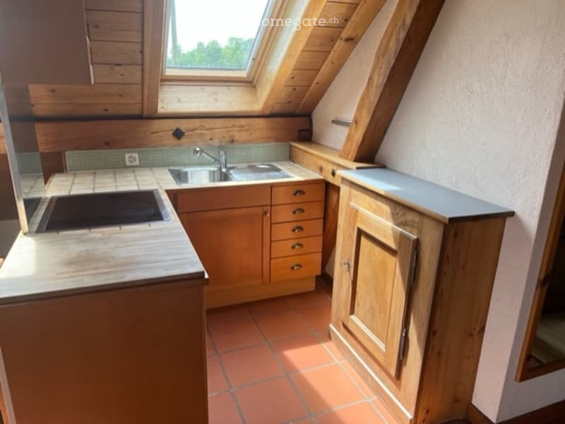 Bright, wooden kitchen with a skylight window, wooden cabinets, a sink, and a stove. The floor is tiled in a warm orange color.