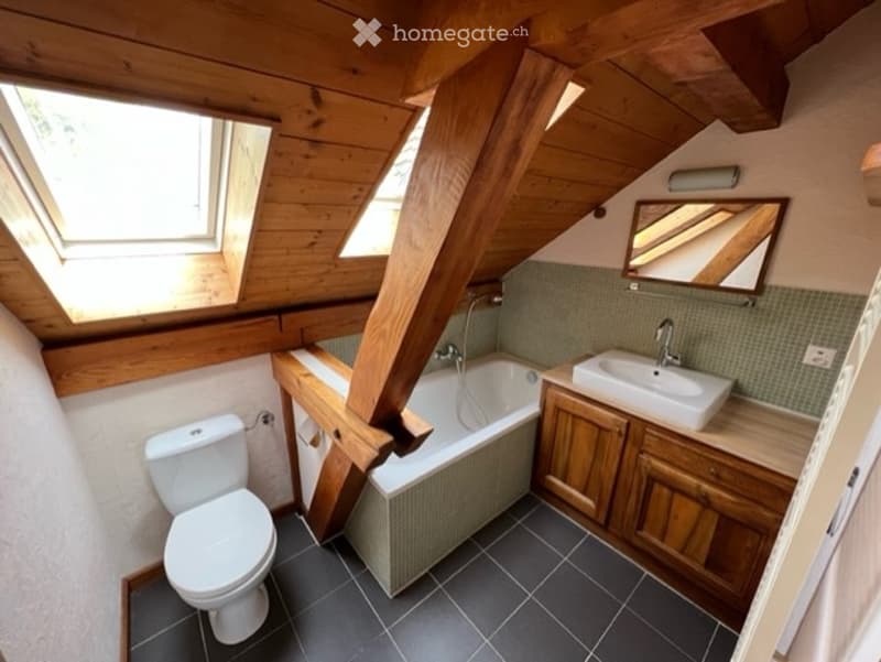 Cozy attic bathroom with wooden beams, skylights, a toilet, a bathtub, a sink, and a mirror.